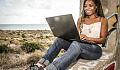 young woman sitting with her back against a tree working on her laptop